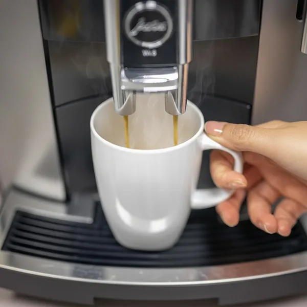 Eine Hand greift sich bei der Kaffeemaschine einen frisch gebrühten Kaffee.